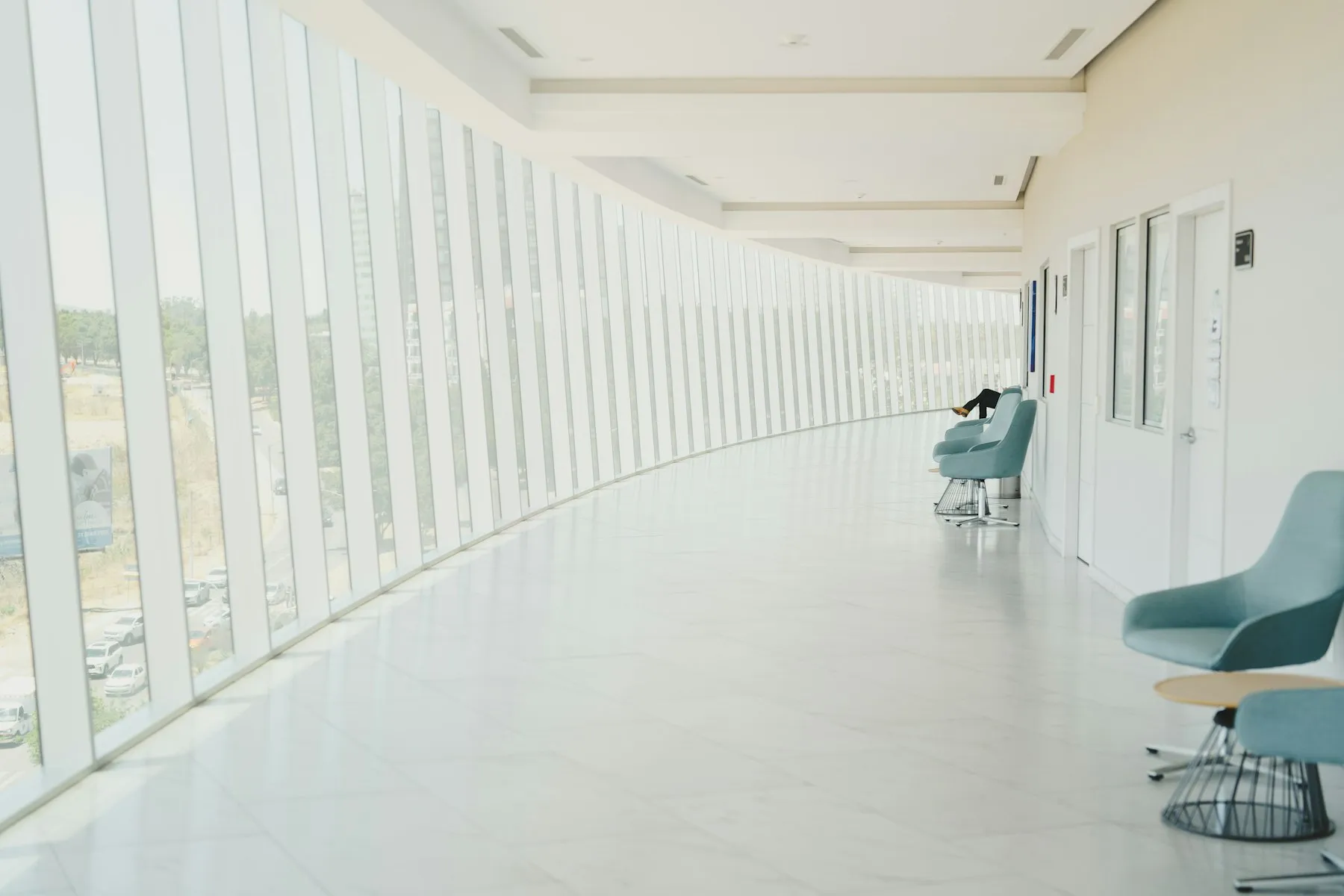 Bright modern healthcare facility corridor with curved curtain-wall glazing and soft-blue waiting chairs