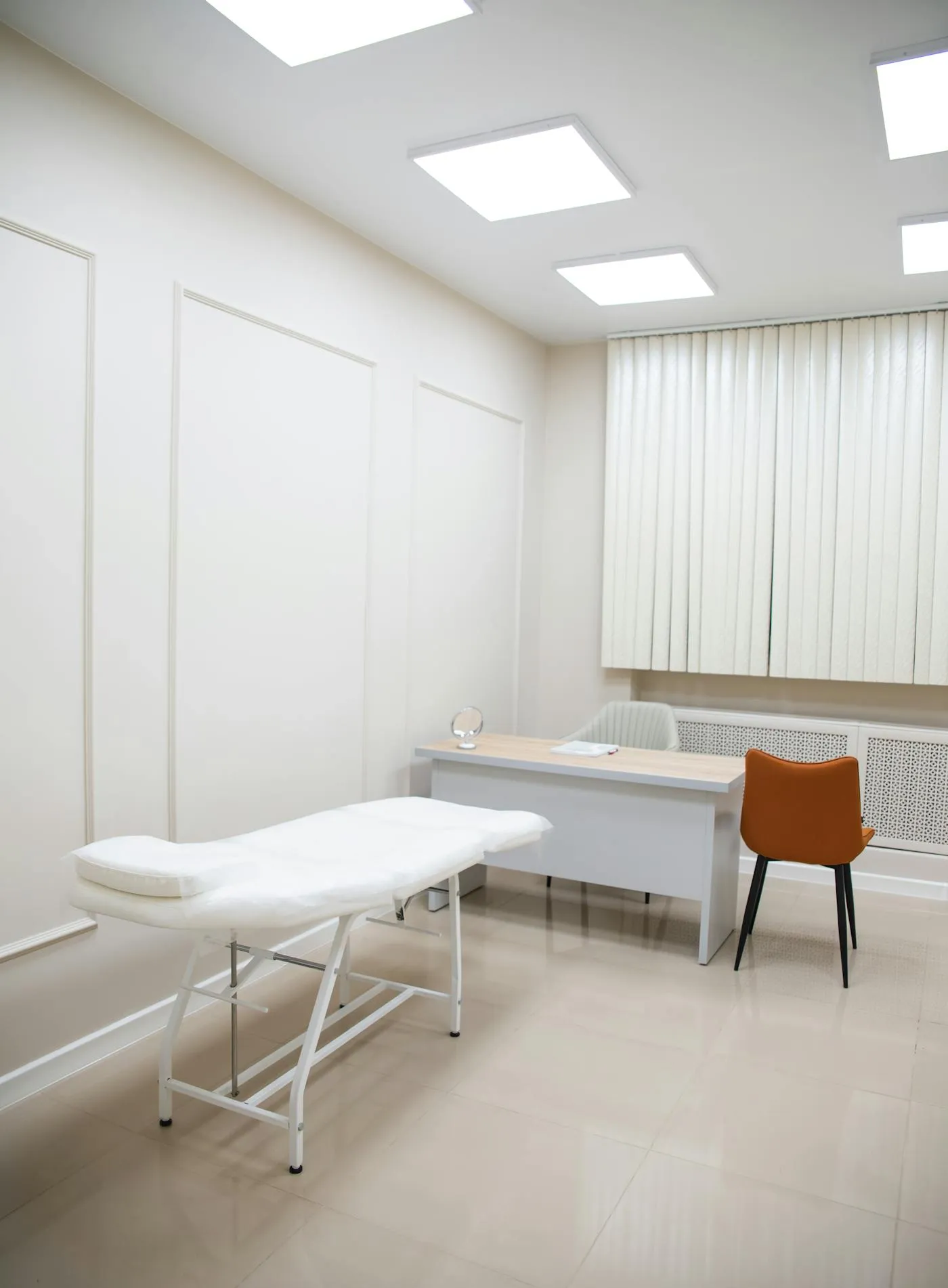 Minimalist private clinic exam room with treatment table, desk, and quiet neutral palette