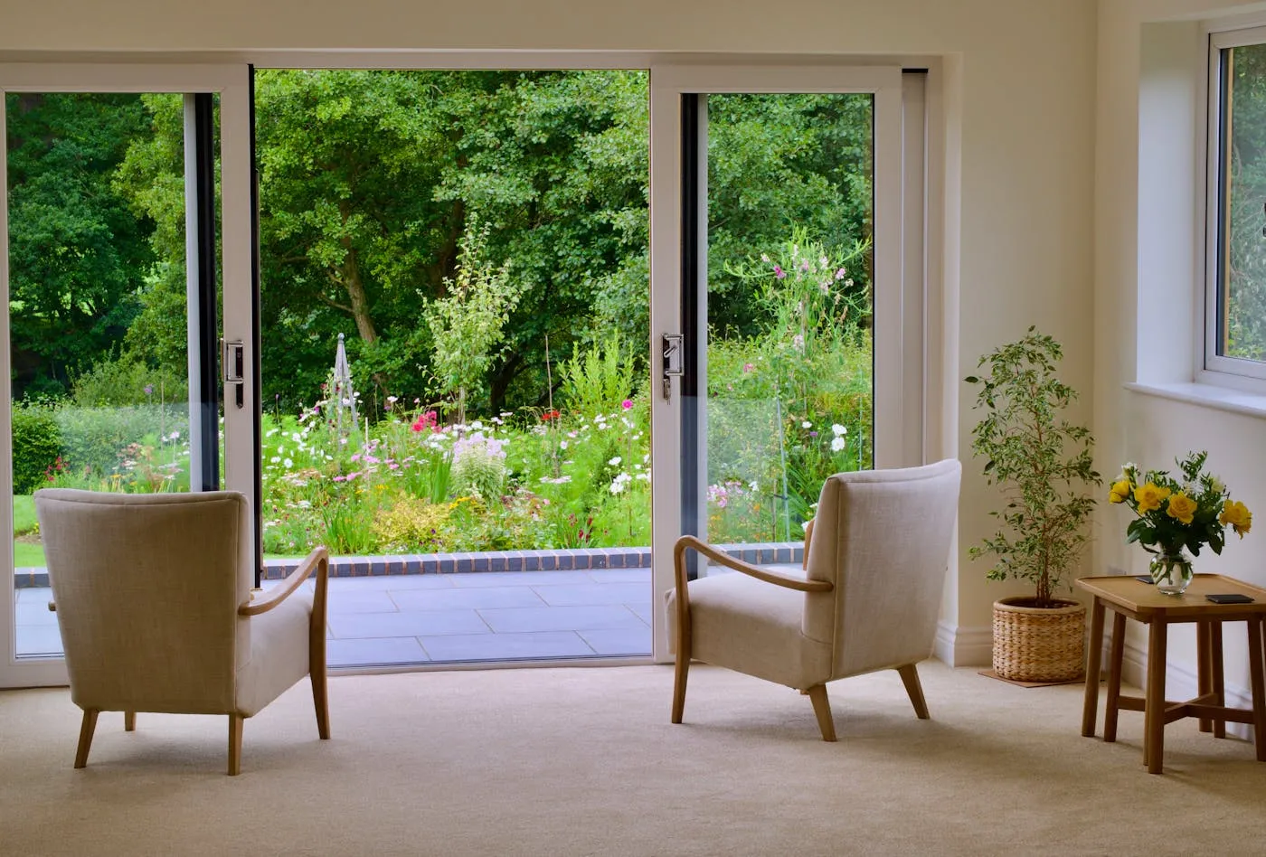 Sunlit care-home common room with two armchairs looking onto a garden through sliding glass doors